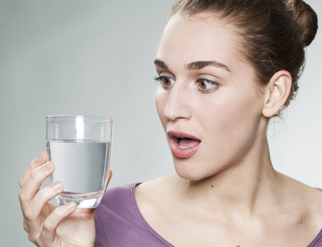 stunned young beautiful woman wearing purple shirt holding glass of pure tap water
