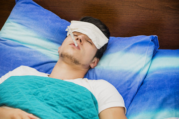 Young man in bed measuring fever with thermometer
