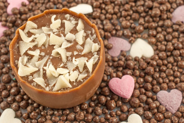 Delicious truffle decorated with white chocolate shavings on chocolate balls and small sugar hearts as background