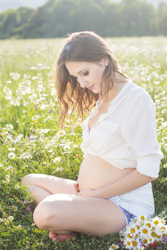 Pregnant smiling woman on the nature in sunset lights