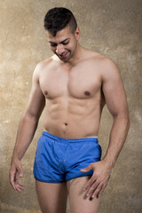 Shirtless strong man posing in swimsuit looking his abdominal muscle and smiling