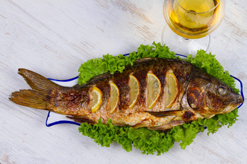 Whole grilled fish carp served with salad and lemon; glass of wine