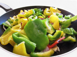 Green, yellow peppers and onions chopped in the cooking pan on white background. The vegetables still need to be cooked