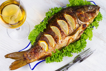 Whole grilled fish carp served with salad and lemon; glass of wine