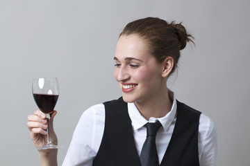 Beautiful young woman wearing uniform of wine waitress looking at aspect and color of red wine
