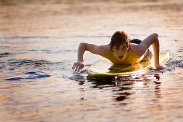 teen boy on a surf board at sunset