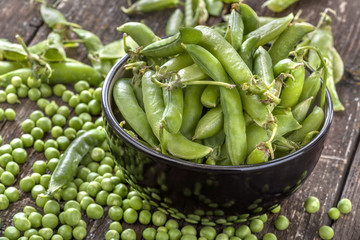 .peas in pods in black bowl on a wooden table