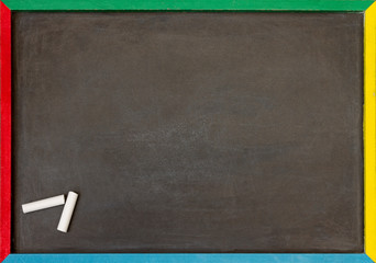 Blank chalkboard with multi coloured frame with two pieces of chalk in the corner