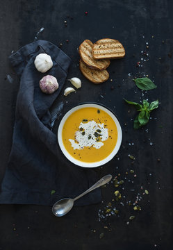 Pumpkin soup with cream, seeds, bread and fresh basil on grunge
