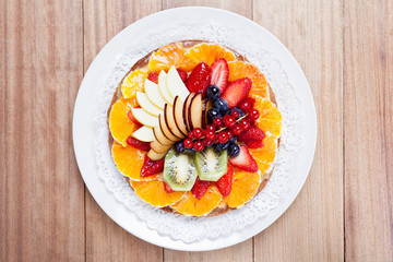 Delicious fruit cake with cream and various types of fruit on a wooden table, top view