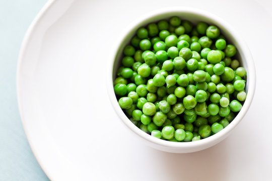 Cooked Green Peas, white bowl and plate, from above. 