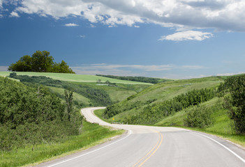 Fototapeta na wymiar a curved paved highway that runs between beautiful green rolling hills with green trees under a blue sky with clouds in the summer time