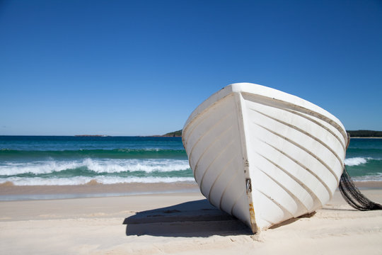 White fishing boat on sand with blue sky and water