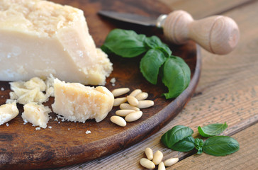 Parmesan, Parmesanmesser, Basilikum, Pinenkerne auf Holzbrett