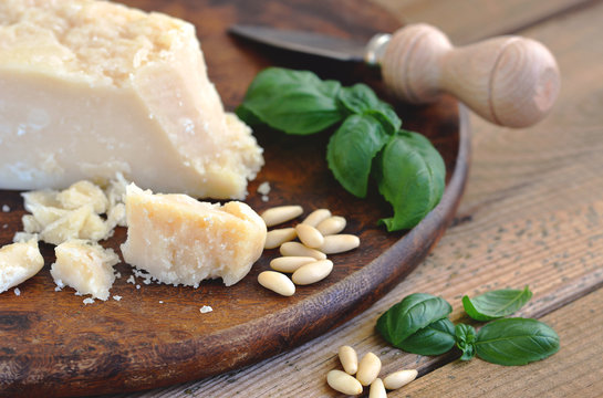Parmesan, Parmesanmesser, Basilikum, Pinenkerne auf Holzbrett