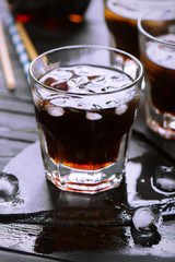 Cola with ice cubes in glasses on dark wooden background. Selective focus