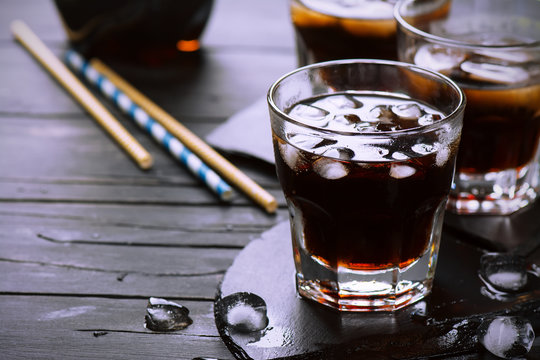 Cola with ice cubes in glasses on dark wooden background. Selective focus