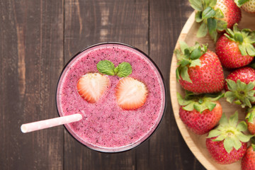 Strawberry smoothie in glass and fresh strawberries on wooden ba