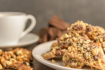 Homemade chocolate toffee nut cookies on a white plate with a ingredients and a cup of coffee in the background on a dark rustic wood table.