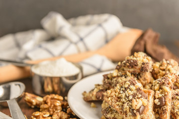 Homemade chocolate walnut cookies with ingredients and kitchen utensils on a dark rustic wood table.