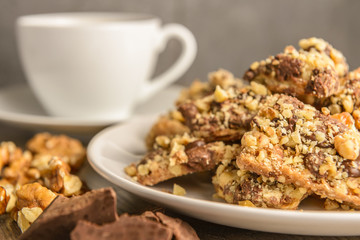 Homemade chocolate toffee nut cookies on a white plate with a ingredients and a cup of coffee in the background on a dark rustic wood table.