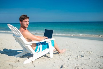 Man using laptop on deck chair at the beach