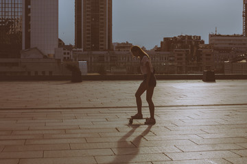 cool young and beautiful caucasian blonde hipster skater girl wearing denim shorts posing smiling and having fun outside while skating with her cute little skateboard summer day