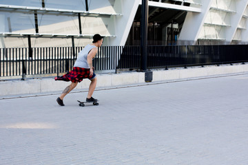 cool young and handsome caucasian brunette hipster skater guy wearing a hat posing smiling and having fun outside while skating with his skateboard during amazing summer day in the city