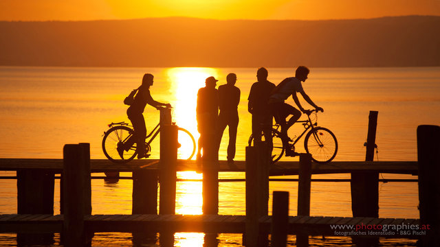 Menschengruppe (Fussg&auml;nger und Radfahrer) im Gegenlicht auf einem Steg am Neusiedlersee - Podersdorf.