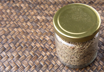 Dried rosemary herb in a mason jar on wicker background