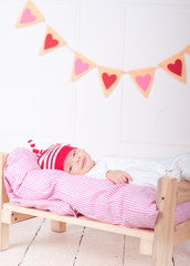 Obraz na płótnie Canvas Cute smiling baby lying on soft bed with hearts on background. Valentines decorations. 