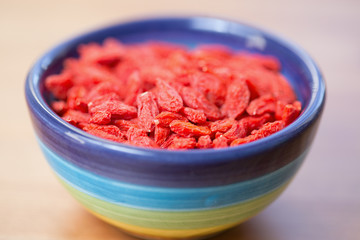Dried goji berries in colored bowl on wooden table
