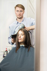 Young woman having her haircut by a handsome hairdresser