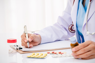 close up of doctor writing record on folder while holding medicine in office