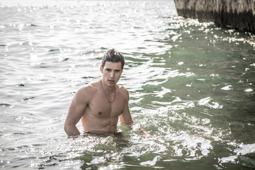 Young shirtless athletic man standing in water by ocean shore