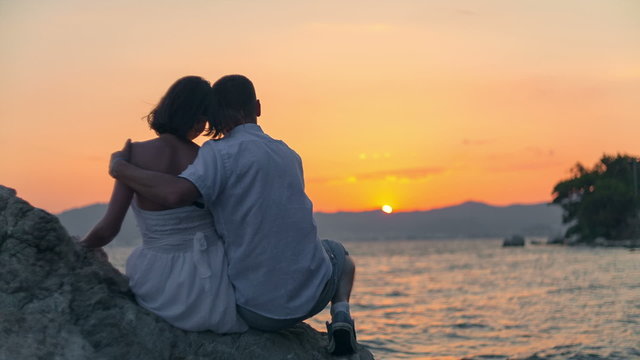 Young couple sit on the rock and wait for sunset. RAW video