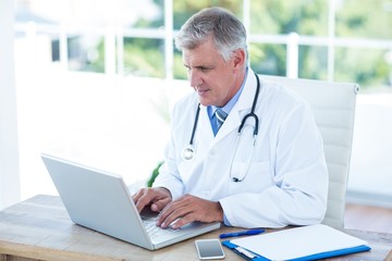 Serious doctor working on laptop at his desk