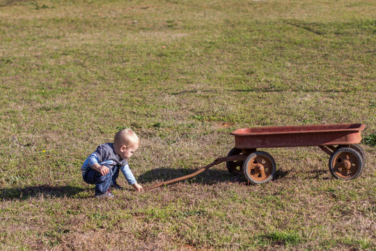 Small Boy Child With An Old Antique Red Wagon In A Yard