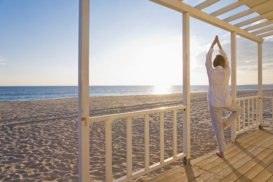 Portugal, Algarve, woman doing yoga exercises at beach house at sunset