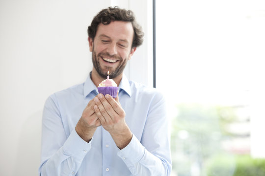 Smiling businessman holding birthday cupcake