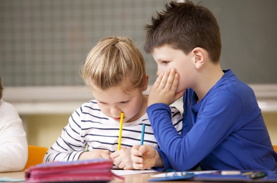 Schoolgirl writing while boy is whispering in here ear