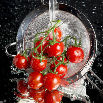 Cherry tomatoes in a colander being washed on a mirror face