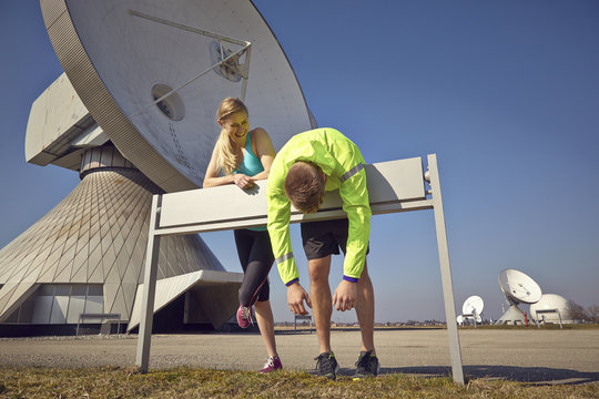 Germany, Raisting, young jogger couple having a rest at ground station