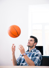 Happy businessman throwing ball in office