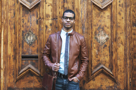 Portrait of businessman wearing leather jacket and glasses in front of wooden door