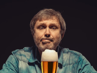 The spellbound man in denim shirt with glass of beer