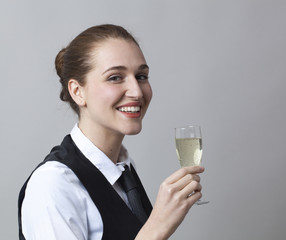 Beautiful young woman wearing uniform of wine waitress happy to raise Champagne glass, profile view