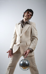 Low angle portrait of a retro man in a 1970s leisure suit and sunglasses holding a disco ball - mirror ball between his legs