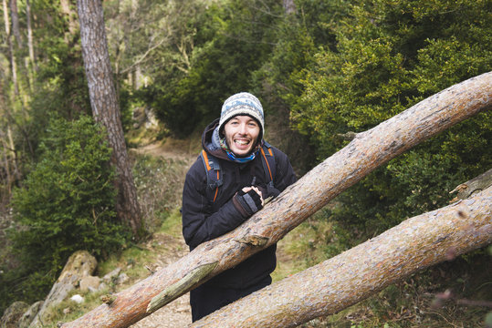 Happy young man leaning against tree trunk in the forest