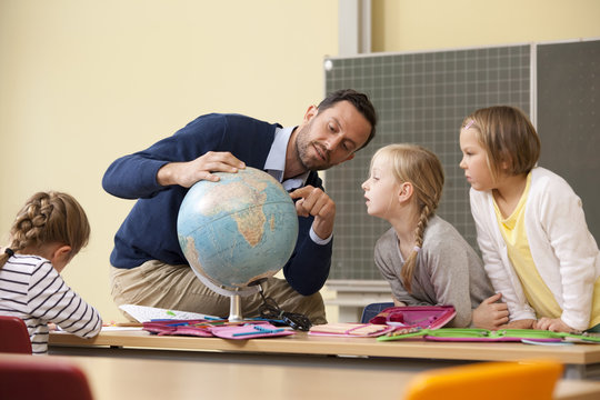 Teacher and pupils looking at globe in classroom